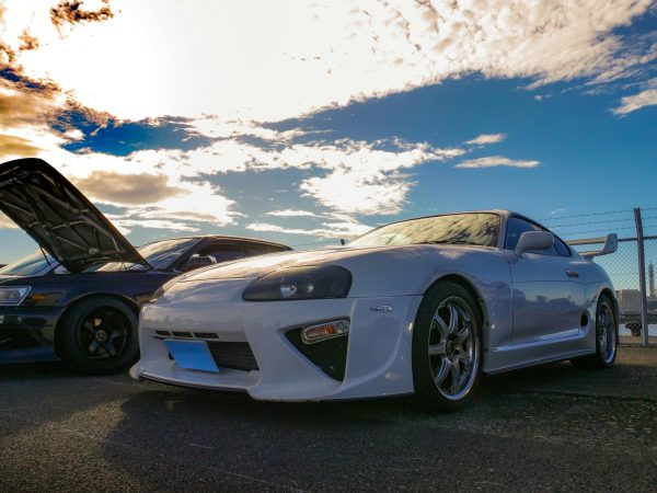 Captivating photo of JDM culture featuring a Toyota Supra at a vibrant car meet under a stunning sky.