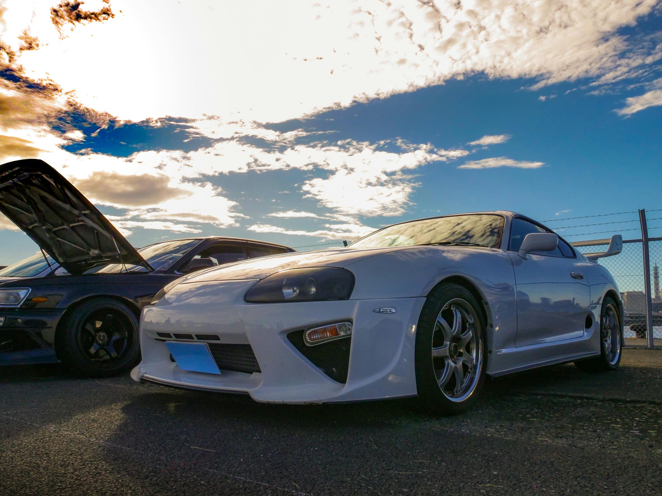 Captivating photo of JDM culture featuring a Toyota Supra at a vibrant car meet under a stunning sky.